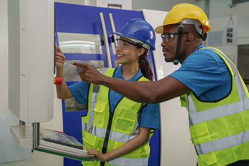 industrail background of asian female factory technician working together with african american male worker at cnc machine control panel at lethe factory