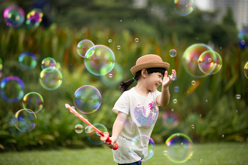 asian chinese young girl blowing bubbles at public park enjoying playing