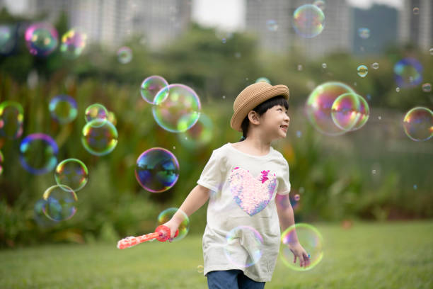 azjatycka chińska młoda dziewczyna dmuchanie pęcherzyki w publicznym parku ciesząc się grając - bubble wand child blowing asian ethnicity zdjęcia i obrazy z banku zdjęć
