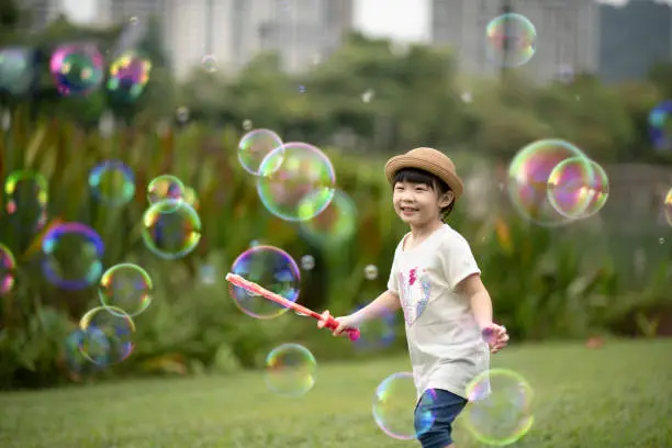Photo of asian chinese young girl blowing bubbles at public park enjoying playing