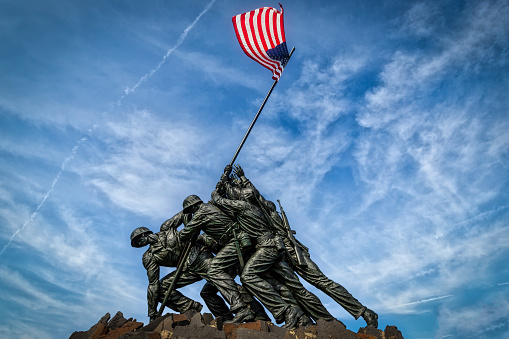 Arlington, Virginia / USA - September 7, 2018: The US flag waves over the US Marine Corps War Memorial designed by sculptor Felix de Weldon and architect Horace W. Peaslee which was unveiled on November 10, 1954.