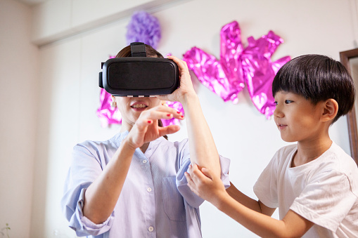 A boy holding hands with a mother wearing VR gogglesMother wearing VR goggles is playing happily with her children