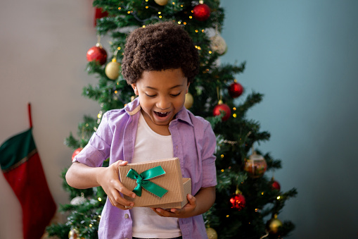 Happy African American boy opening a Christmas gift at home and looking surprised - holidays concepts