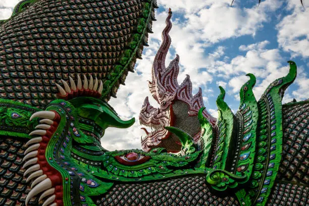 Huge and vibrant-colored great naga sculpture from side view in Buddhist temple against white cloudy sky. Wat Baan Den.