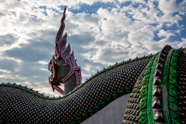 Huge and vibrant-colored great naga sculpture from rear view in Buddhist temple against white cloudy sky. Wat Baan Den.