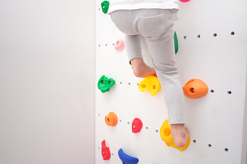 Close up of legs of little kindergarten boy having fun trying to climb on a small rock wall indoor at home, Physical, Hand and Eye Coordination, Sensory, Motor Skills development, Home workout concept