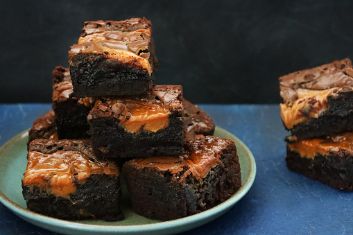 Stock photo showing close-up view of green plate containing a heap of homemade chocolate salted caramel brownies cut into square slices.
