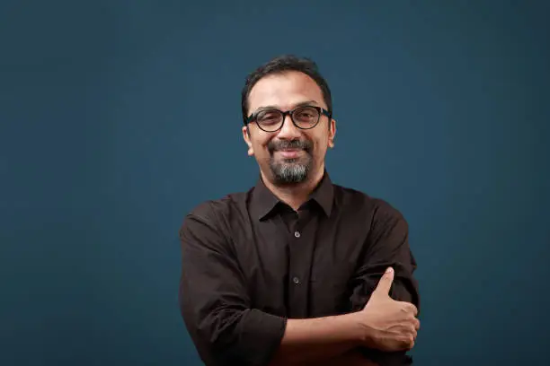 Portrait of a smiling man of Indian ethnicity against a blue wall background.
