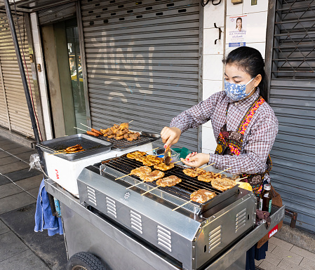 Bangkok, Thailand - February 28th, 2020: A traditional street food vendor, selling grilled meat on a stick, on a Bangkok street.
