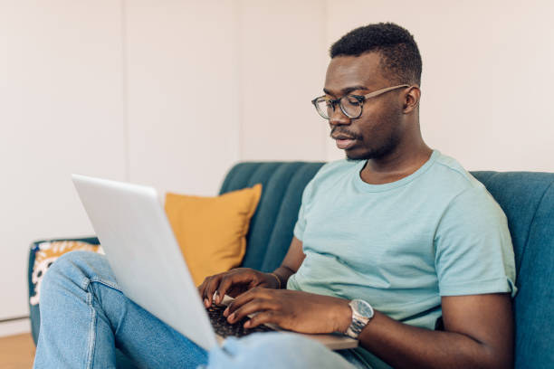 istock Young African-American man sitting on the couch and working 1277984458