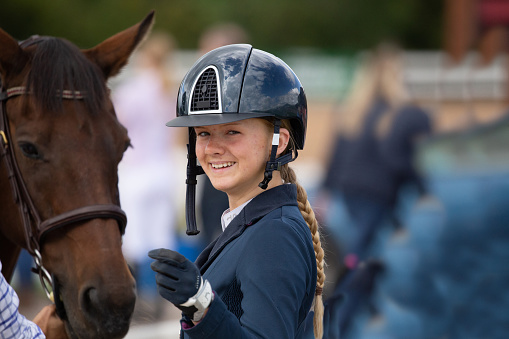 Happy, smiling young horsewoman in a protective riding helmet stood by her horse.