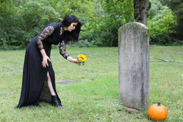 frau in schwarz stellt helle sonnenblume auf vergessenes grab. - spooky cemetery single flower flower stock-fotos und bilder