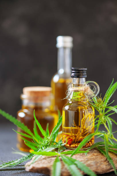 Oil in bottle and leaves of hemp on a stone podium on dark background. Oil in bottle and leaves of hemp on a stone podium on dark background. cannabidiol photos stock pictures, royalty-free photos & images