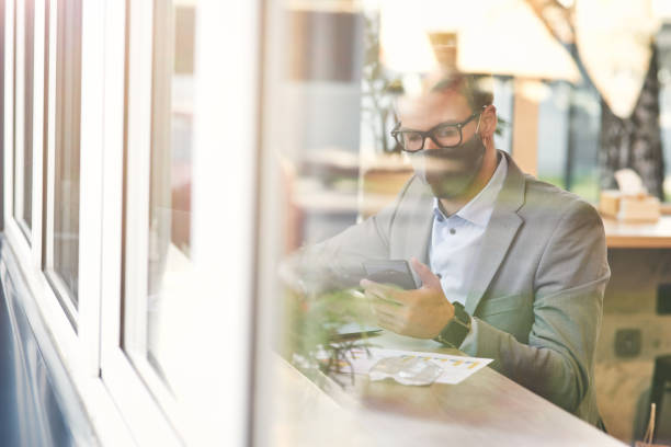 istock Work during covid 19 outbreak. Young businessman or male freelancer wearing protective face mask using smartphone while working remotely in cafe 1277990236
