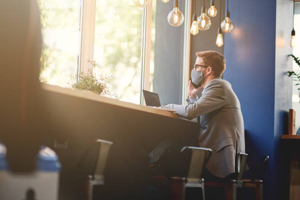 istock Young businessman wearing protective face mask talking by phone while working remotely in cafe during covid 19 outbreak 1277990263