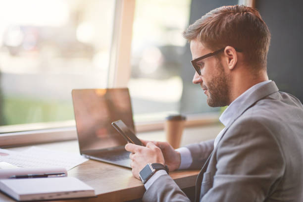 istock Side view of a young businessman or male freelancer using his smartphone while working online remotely in cafe 1277990328