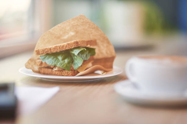 A cropped shot shows a woman's hand holding a piece of toasted egg sandwich, ready to take a bite. The scene captures a peaceful morning breakfast, with a cup of coffee latte nearby, adding a warm and cozy feel to the setting. The golden-brown toast and creamy latte make for a perfect, healthy start to her day.