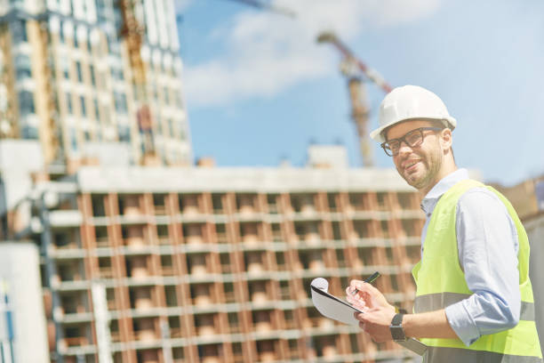 istock Young civil engineer or construction supervisor wearing helmet smiling at camera while inspecting building site and making some notes 1277990552