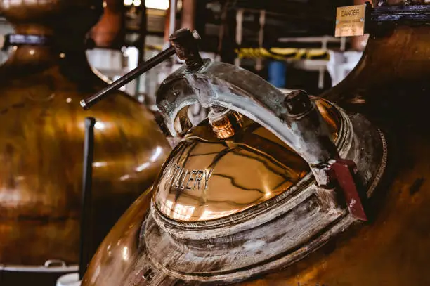 Detail of the inspection and fill port of a copper still in a scotch distillery.  Second still is out of focus in the background.