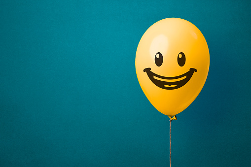 Stock photo of a yellow balloon with happy face on a blue background and copy space. Joy and happiness concept
