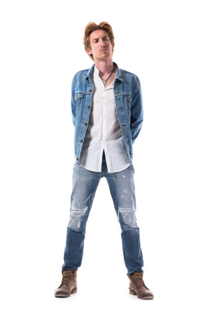 Stylish young male fashion model with red hair in jeans looking away with hands on back. Stylish young male fashion model with red hair in jeans looking away with hands on back. Full body isolated on white background. hands behind back stock pictures, royalty-free photos & images