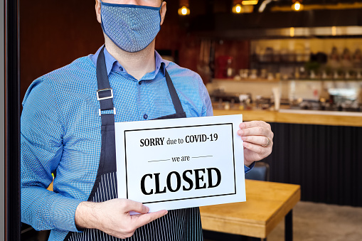 Businessman closing business activity due to covid-19 emergency lockdown quarantine – Owner with protective face mask at restaurant entrance holding closing sign due to coronavirus – Bankruptcy store