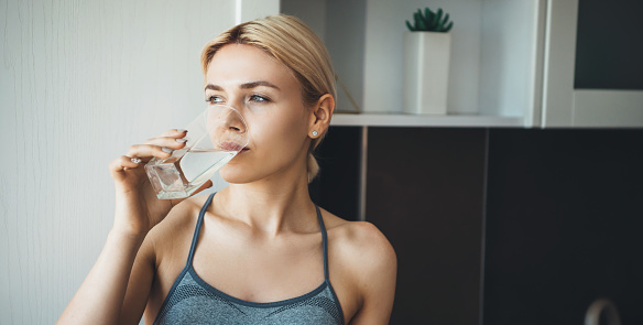 Joven mujer de fitness beber agua después de ejercicios de yoga usando ropa deportiva en casa en la cocina photo