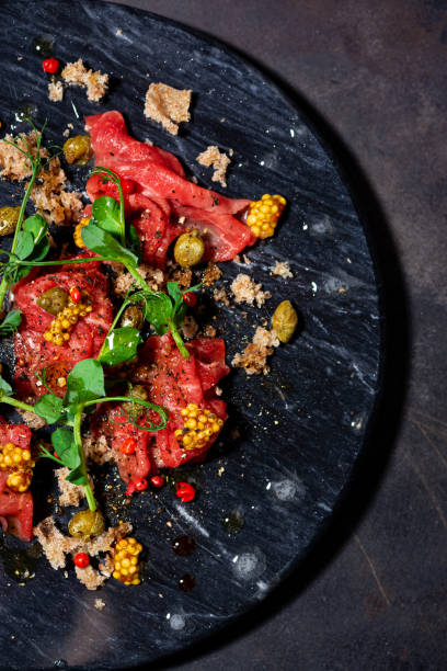 istock fresh beef carpaccio with capers, mustard and arugula on black board, vertical top view 1278006281