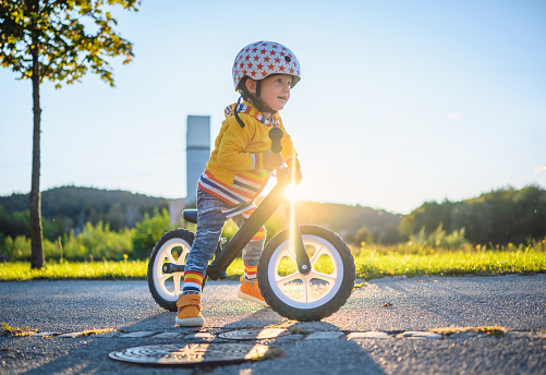 Caucasian boy with sports helmets driving balance bike outdoors on a sunny day. He is learning new skill.