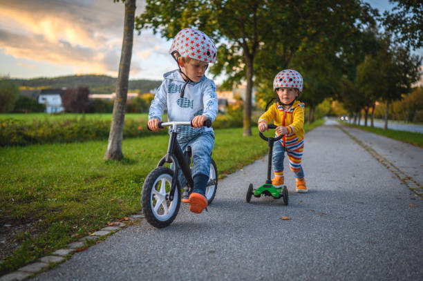 fratelli caucasici guidano equilibrio bici e spingere scooter all'aperto - 5549 foto e immagini stock