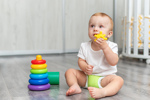 A baby is playing on the floor. The child is sitting on the floor. The kid takes the toy in his mouth and licks it.