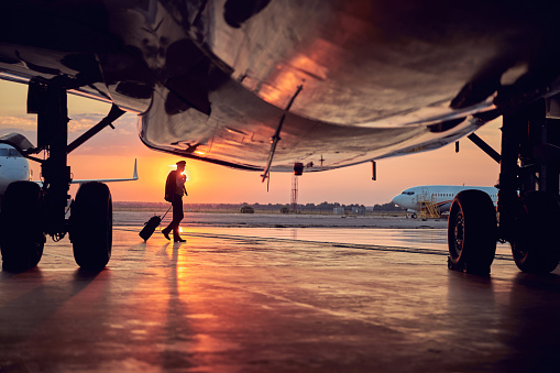 Full length portrait of part of passenger airplane with pilot isolated on sunset background