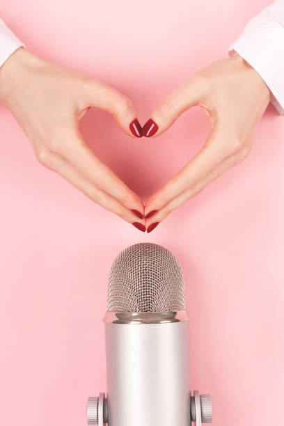 istock Woman hands in a heart shape and a microphone on pink background. 1278013583