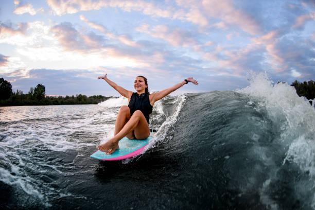 istock cheerful woman riding wave while sitting on surf style wakeboard with outstretched arms 1278022155