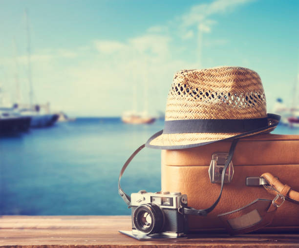 Vintage suitcase and photo camera. Summer travel and cruise concept. Vintage suitcase, hipster hat, photo camera and passport on wooden dack. Tropical sea, beach and yachts in background. Summer holiday  and cruise traveling concept. yacht photos stock pictures, royalty-free photos & images