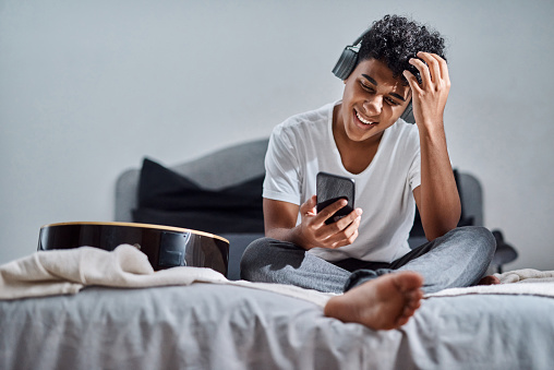 Shot of a young man using a smartphone and headphones to listen to music at home