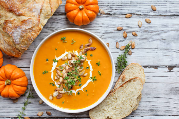 Pumpkin Soup with Sour Cream Thyme and Artisan Bread Fresh pumpkin soup garnished with sour cream, toasted pumpkin seeds and thyme with homemade artisan bread over a white wood background. Flatlay. pumpkin soup photos stock pictures, royalty-free photos & images
