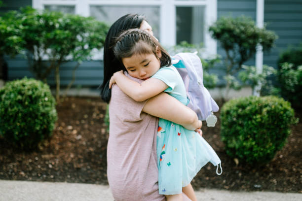 Girl Hugs Her Mother On First Day of School A Korean woman holds her daughter tightly in an embrace, the girl feeling anxious going back to school. preschool student photos stock pictures, royalty-free photos & images