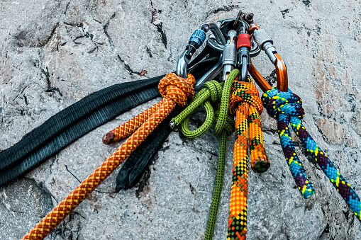 Different colourful static ropes hanging on the carabiners nailed in the rock of the canyon.