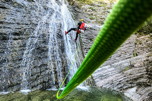 Canyoneering male adventurer seen from below rappelling down the waterfall in an amazing canyon in Montenegro.