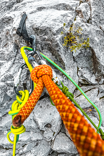 Orange, yellow and green rope all prepared and secured for rappelling down the cliff while orange one is a safety rope hooked up with carabiner to an anchor.