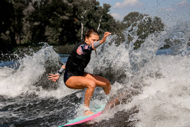 schöne frau steht mit gebeugten knien auf surf-stil wakeboard und reiten auf welle - knees bent stock-fotos und bilder