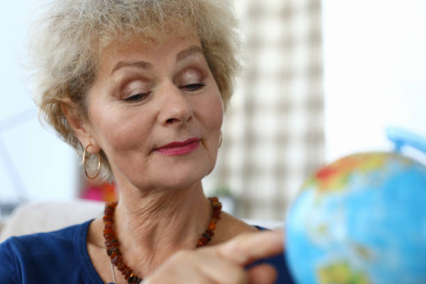 istock Elderly woman in apartment shows finger on globe 1278050034