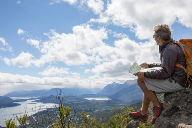 istock Male hiker relaxes on cliff edge, reading map 1278053652