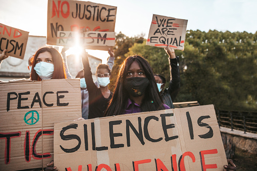 Anti-Racism protest with facefask to protect Covid-19 pandemic spread. Protestors holding hand-made signs on cardboards.