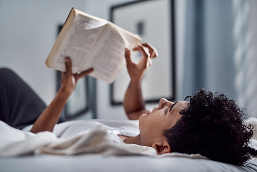 Shot of a young man reading a book and relaxing on his bed at home