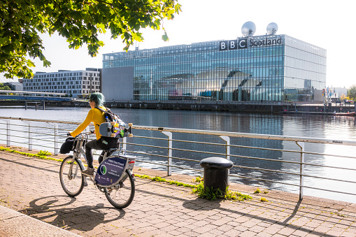 Glasgow, Scotland - A cyclist passes on the Clydeside path, with the BBC Scotland headquarters building on the other side of the Clyde.