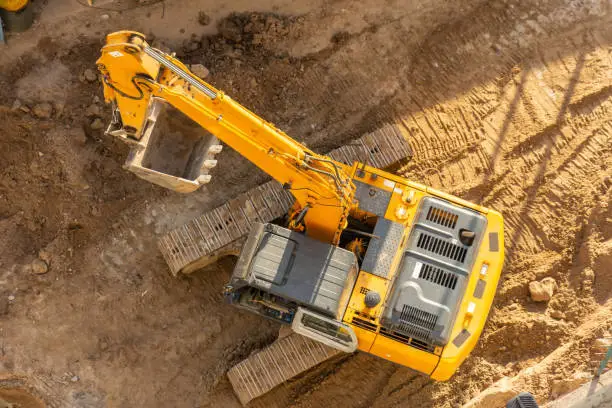 Photo of Excavator on the ground of a construction site with a raised bucket, top aerial view.