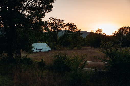 Small white Camper Van - Motor Home parked on dry meadow close to pine trees in sunset twilight light. Dalmatia, Croatia, Southeast Europe.