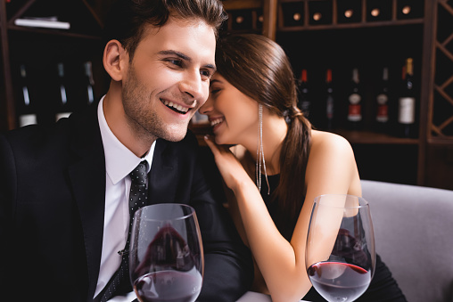 Selective focus of elegant woman embracing boyfriend in suit near glasses of wine in restaurant